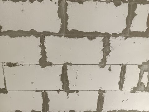 Close-up of a textured wall made of aerated concrete wall with visible mortar joints. The surface appears unfinished and rough, showcasing construction materials.