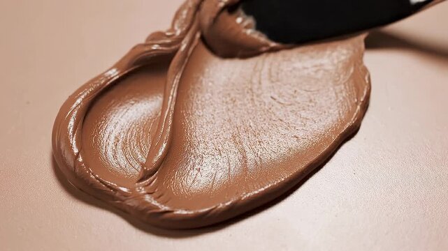 Motion of creamy white cosmetic texture smears concept. Smooth creamy chocolate spread with a knife on a beige surface close up