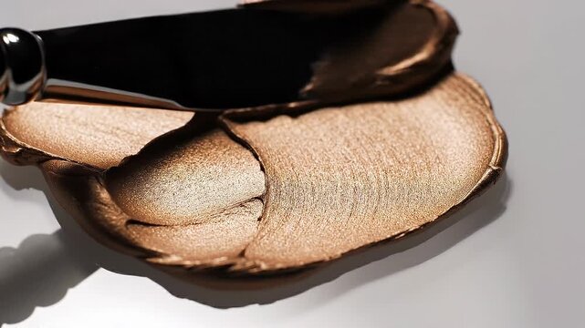 Close up of metallic bronze makeup cream texture with applicator knife on white background