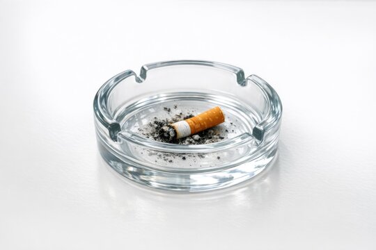 A cigarette in an empty glass ashtray on a table