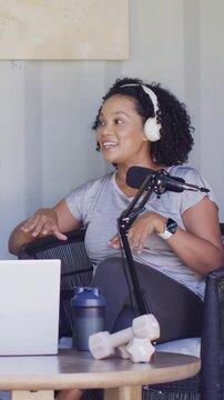 Vertical video: Leaning host with phones talking into mic in studio recording show with weights