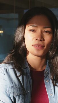Vertical video: Reacting to offscreen remark, woman smiling, laughing in warm room, denim shirt