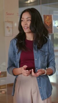 Vertical video: Answering offscreen question, woman in denim shirt explaining by board, smiling
