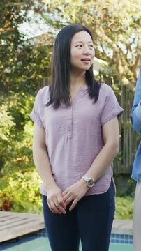 Vertical video: Listening mature Chinese woman in lilac top responding to gesturing speaker by pool