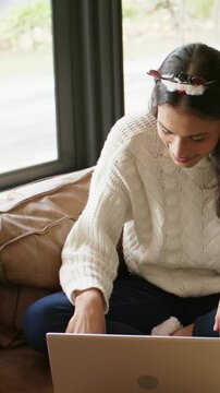 Vertical video: Leaning woman in sweater and headband adjusting laptop on couch after companion tap