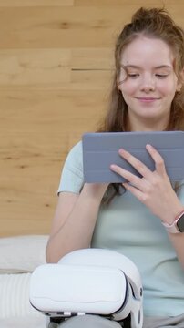 Vertical video: Raising tablet, woman in mint top adjusting and scrolling on sofa with headset