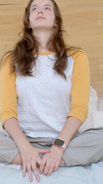 Vertical video: Opening eyes, woman wearing yellow raglan lifting head back on bed, smartwatch