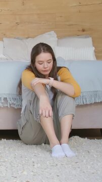 Vertical video: Glancing woman in mustard top checking smartwatch fixing sleeve by bed rug at start