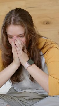 Vertical video: Hands covering, woman sitting looking down at home with pink watch, mustard tee