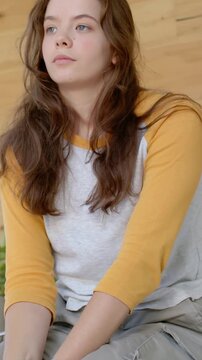 Vertical video: Turning gaze, woman sitting, shifting left by wood wall, raglan top and cargo pants