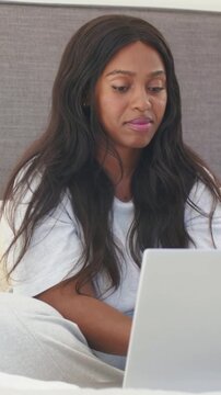 Vertical video: Glancing at laptop, woman in white T-shirt typing on sofa at home, reading content