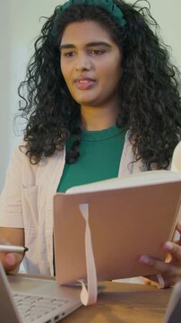 Vertical video: Opening pink notebook, adult woman practicing talk at home, pointing pen at laptop