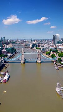 Aerial hyper time lapse view of the city skyline and Tower Bridge in London, England, during a sunny summer day with river Thames boat traffic