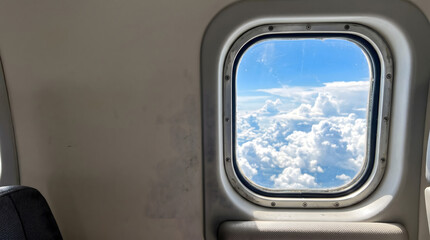 Fototapeta premium Airplane window view above clouds with bright sky and minimal cabin interior copy space composition