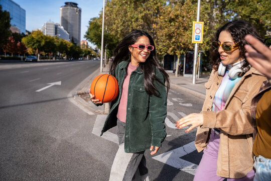 Gen-Z women friends walking in city with basketball