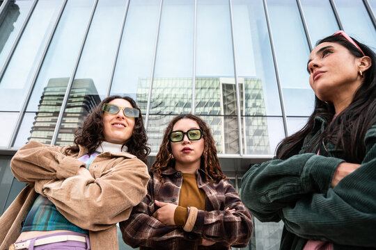 Gen-z women friends posing outdoors by modern glass office