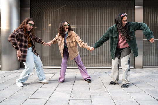 Gen Z female urban dancers holding hands on city street