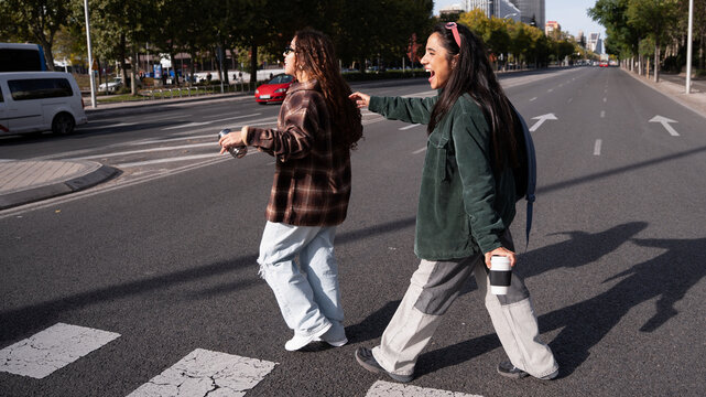 Gen-Z women friends laughing while crossing city street