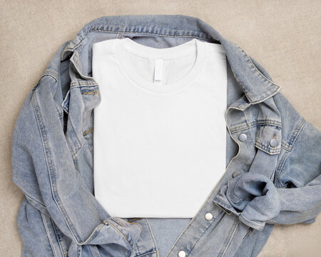 Blank white folded t-shirt mockup over blue denim jacket, crewneck template for print on demand