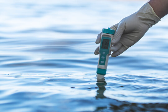 Electronic water testing hand over blurred blue water background, water quality check. testing the level of water pollution in a natural reservoir.