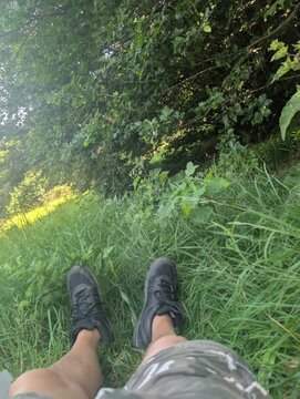 Momento di relax nella natura, con gambe distese sull&rsquo;erba alta e vegetazione rigogliosa sullo sfondo. Una scena tranquilla che trasmette pace, outdoor lifestyle e connessione con l&rsquo;ambiente