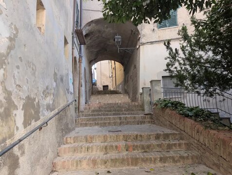 Scalinata in pietra in un vicolo storico, con muri antichi, arco in mattoni e lanterna sospesa., architettura tradizionale e atmosfera autentica di un borgo Marchigiano