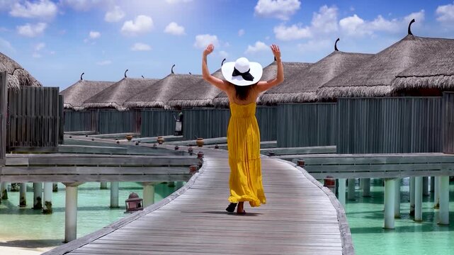 A happy tourist woman with a yellow summer dress walks in the Maldives islands during her holiday time, tropical travel concept