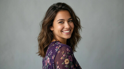 Fototapeta premium A smiling woman with wavy hair turns to look over her shoulder in a studio setting wearing a floral blouse