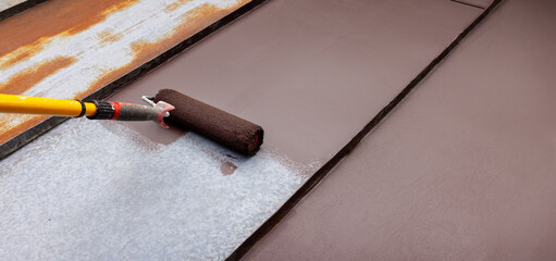 Naklejka premium painting tin metal roof with roller and brown paint. rusty house roofing restoration
