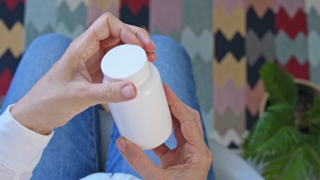 Woman opening white plastic bottle with pills in close-up from above, illustrating capsules for personal wellness. Health support, healthy routine, wellness habits suitable for healthcare and