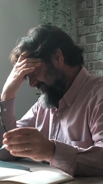 One overworked tired man taking off his glasses and touching his painful head for migraine headache in front of a laptop sitting at the desk. Concept of stress and head ache disturb working computer