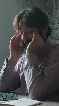 Migraine headache symptoms at home office. One worker adult man stop work on computer sitting at the table for stress. Overworked stressed male people with head ache taking off glass and touch head