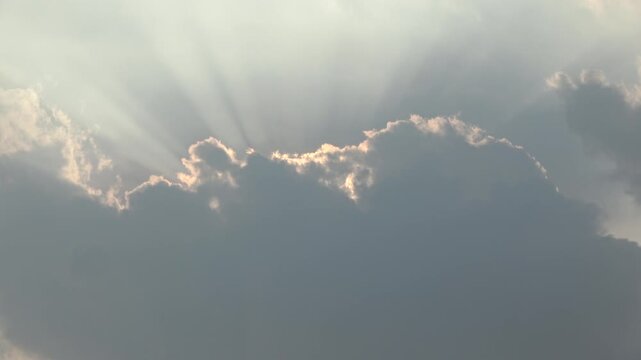 Beautiful video of heavenly sunbeams piercing through thick grey clouds during late afternoon.