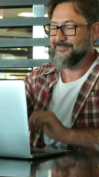 One young mature man with beard and eyeglasses working on a laptop on the table. People enjoy and use technology with computer and internet connection. Alternative workplace for modern adult male