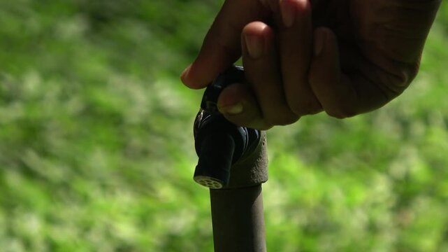 Close up view of a hand trying to turn on a black plastic water spigot on the park.