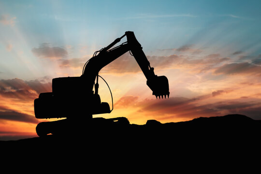 Crawler excavator silhouette digging the soil into a truck ,In the construction site on sunset background