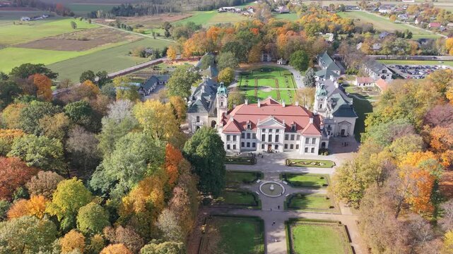 Aerial footage retreating from the historic Zamoyski Palace in Kozlowka, Poland, surrounded by colorful autumn park trees.
