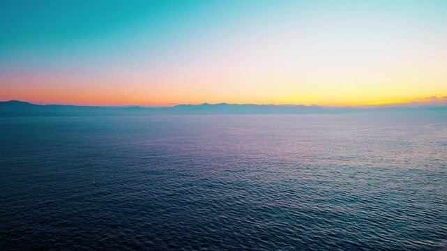 Sunrise over calm ocean with distant mountain horizon