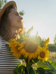 Side profile portrait of a young woman pressing sunflowers to her chest in a field at sunset © olezzo