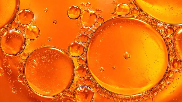 Close up of orange oil bubbles and small emulsions floating in a orange liquid.
