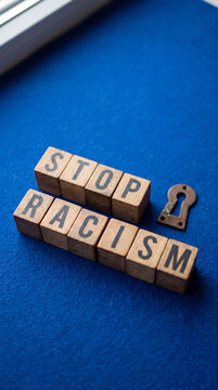 Wooden letter blocks spelling the message stop racism next to a decorative metal keyhole on a textured blue fabric background