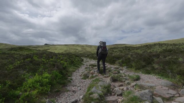 Hiker with big backpack walking up the Devil's Staircase on the West Highland Way in Scotland.
