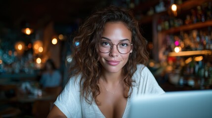 Obraz premium A smiling woman with curly hair sits in a lively café, intently focused on her laptop, embodying a modern, tech-savvy lifestyle filled with creativity and joy in her expression.