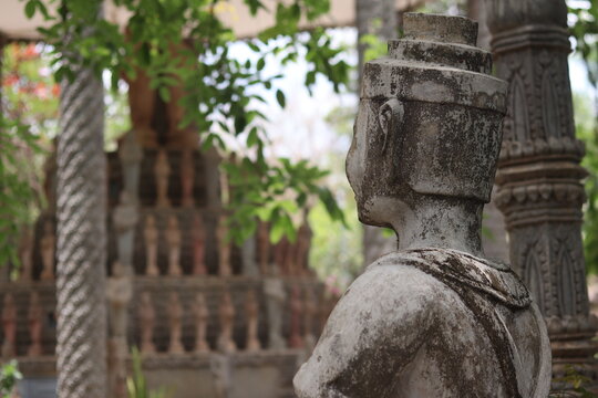 Ancient Khmer Guardian Stone Statue in Profile with Blurred Temple Columns and Green Foliage at Prasat Vimean Koh Pos Kien Svay Cambodia