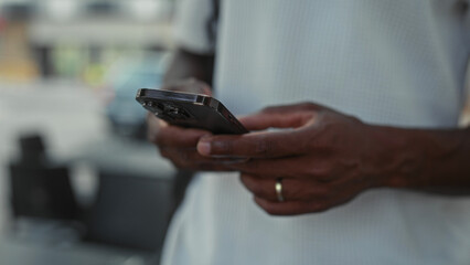 Man holding smartphone with visible hands and wedding ring, wearing white shirt on a city street near cafe tables  digital focus. © Krakenimages.com