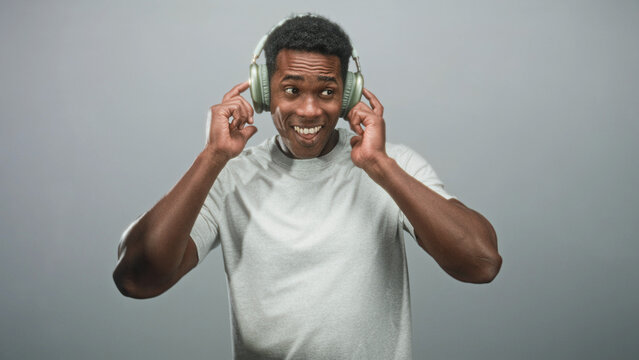 Man with headphones grinning and pointing fingers in gray studio setting with plain backdrop; joy groove.