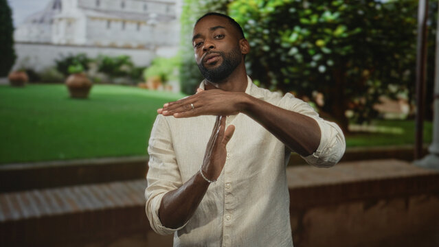 Man forms time out gesture with hands and forearms visible in front of building courtyard; confidence focus determination.