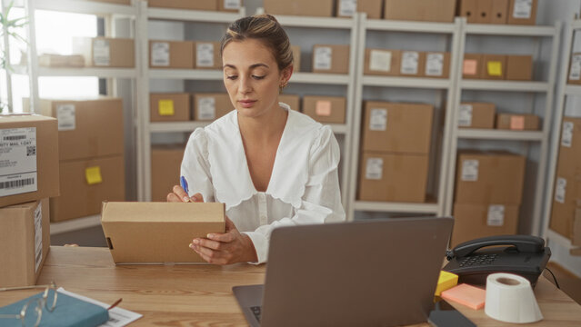 Woman signing a parcel at a desk in a building office filled with shipping boxes and storage shelves; focus efficiency.