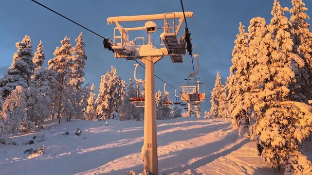 Snowy Ski Lift Surrounded by Frost-Covered Trees in Finnish Lapland. Warm winter sunlight illuminates a frozen Arctic landscape at a ski resort.