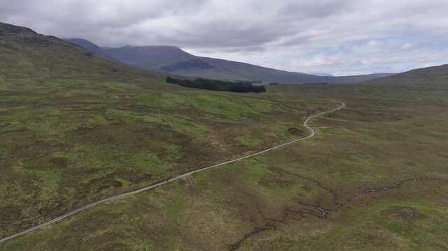 Aerial drone push forward shot of a lone hiker walking on the West Highland Way in Scotland. We walks on a long straight dirt road into the Rannoch moor swamp area 